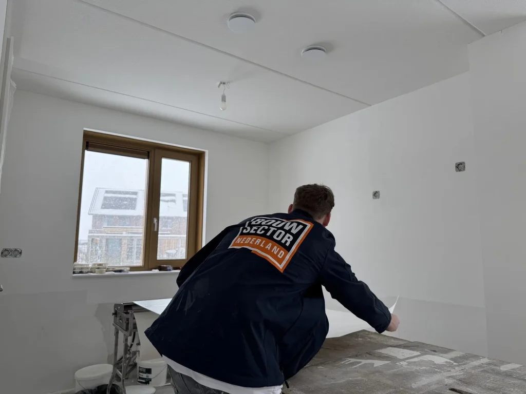 Behanger van Bouwsector Nederland in een donkerblauwe werkjas pakt een baan van de plaktafel in een kale kamer