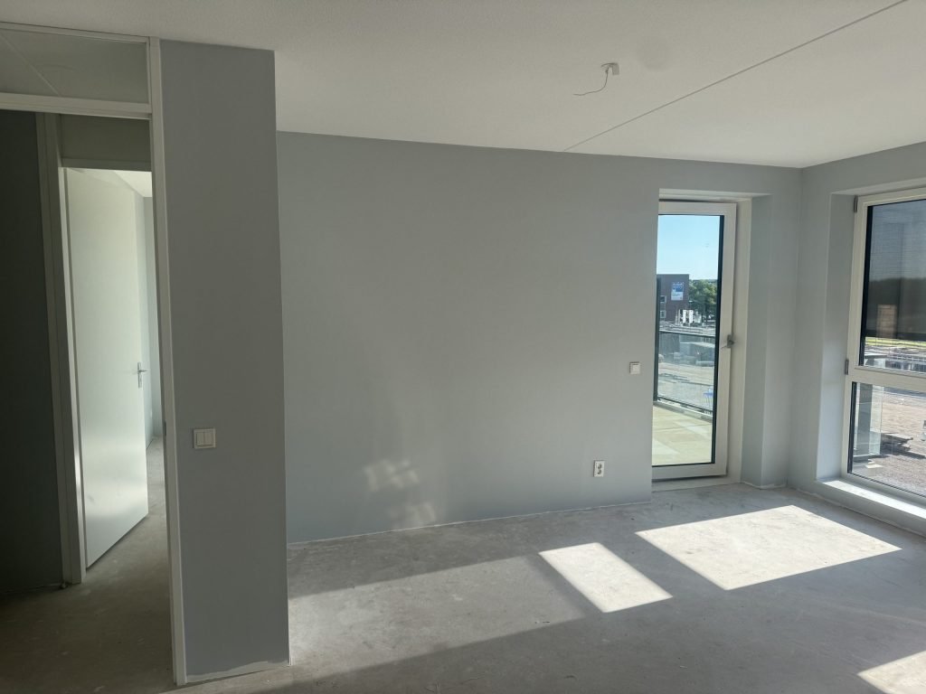 Lichtgrijze woonkamer van een appartement met een balkondeur en een doorgang naar de gang