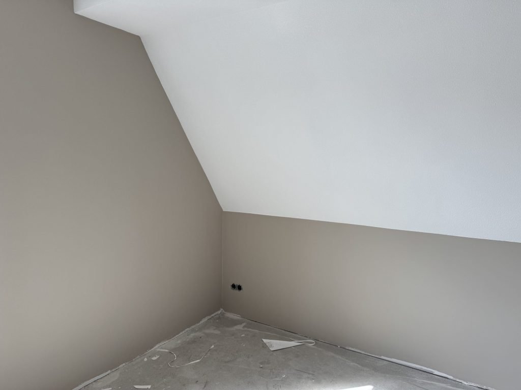 Kamer onder het dak met een schuine wand, gesausde wanden in een zachte beigetint en een wit plafond